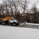 Snow plow truck clearing snow removal leads route on a residential street in winter